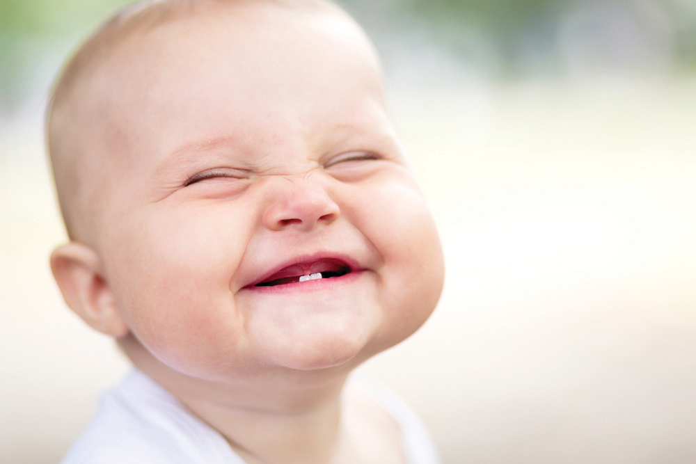 Smiling baby squinting to show his two lower teeth