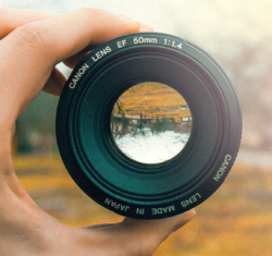 Hand holding up camera lens which shows a reflected autumnal scene