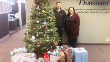 Two Burkhart Associates stand near a tree with gifts ready to go to the The Good Neighbor Center