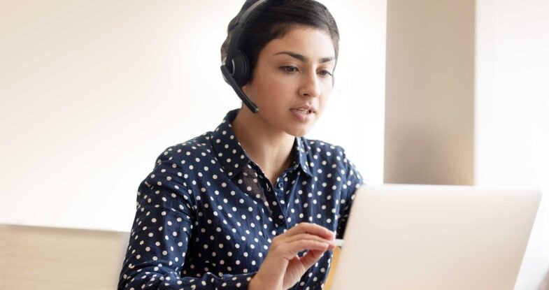 A woman wearing a headset sits at a laptop as she conducts a call.