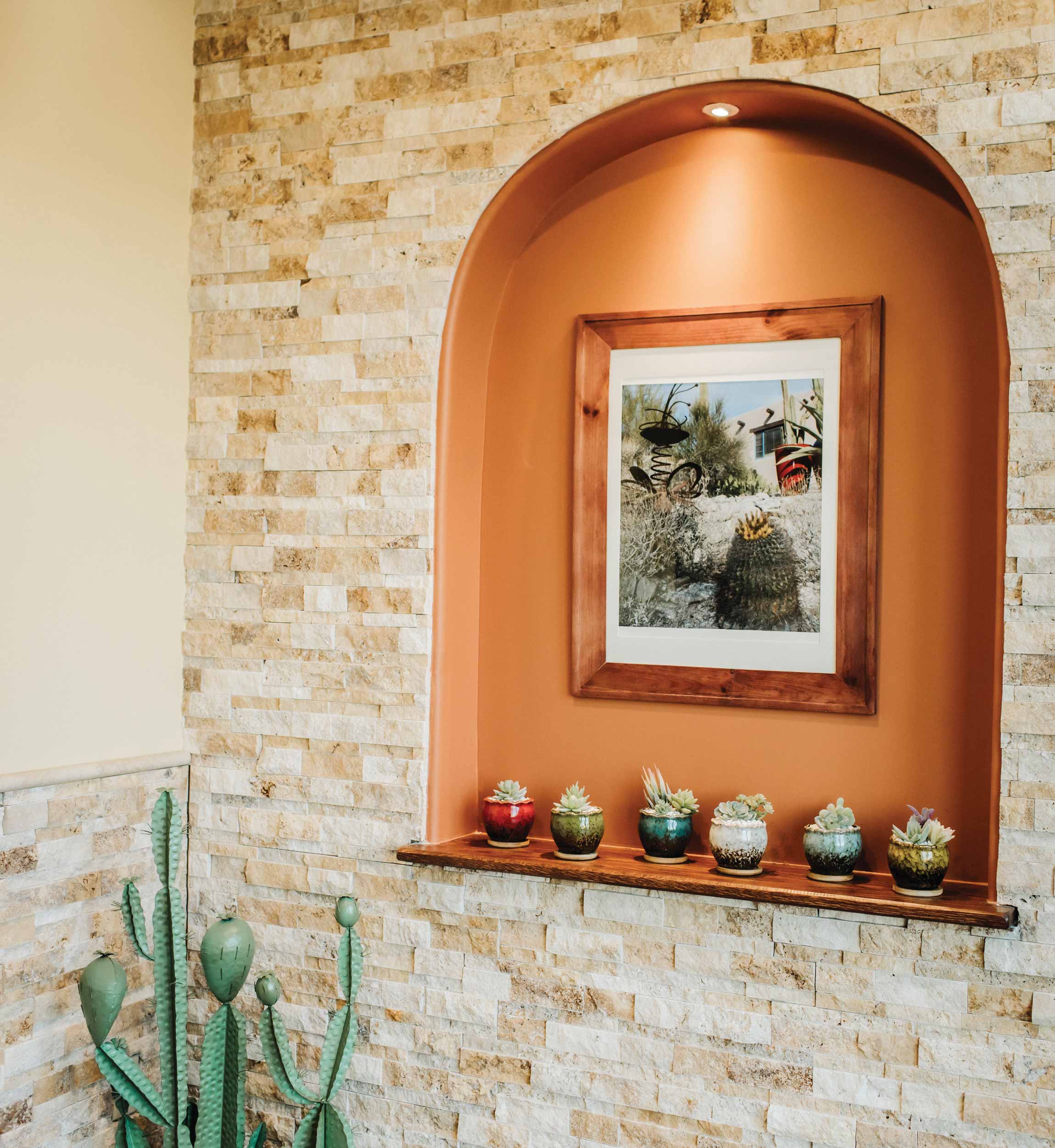 Touches of Santa Fe can be seen throughout the practice, like this niche. The rich, orange-based, clay color draws attention to the photograph showcasing southwestern architecture behind a cactus garden. Six little brightly-potted cacti dance across the shelf.