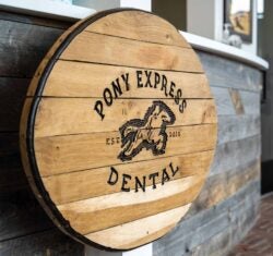 A wooden, 3D, real-life interpretation of the Pony Express Dental logo, burned into the light colored rough wood, greets patients as they enter the practice.