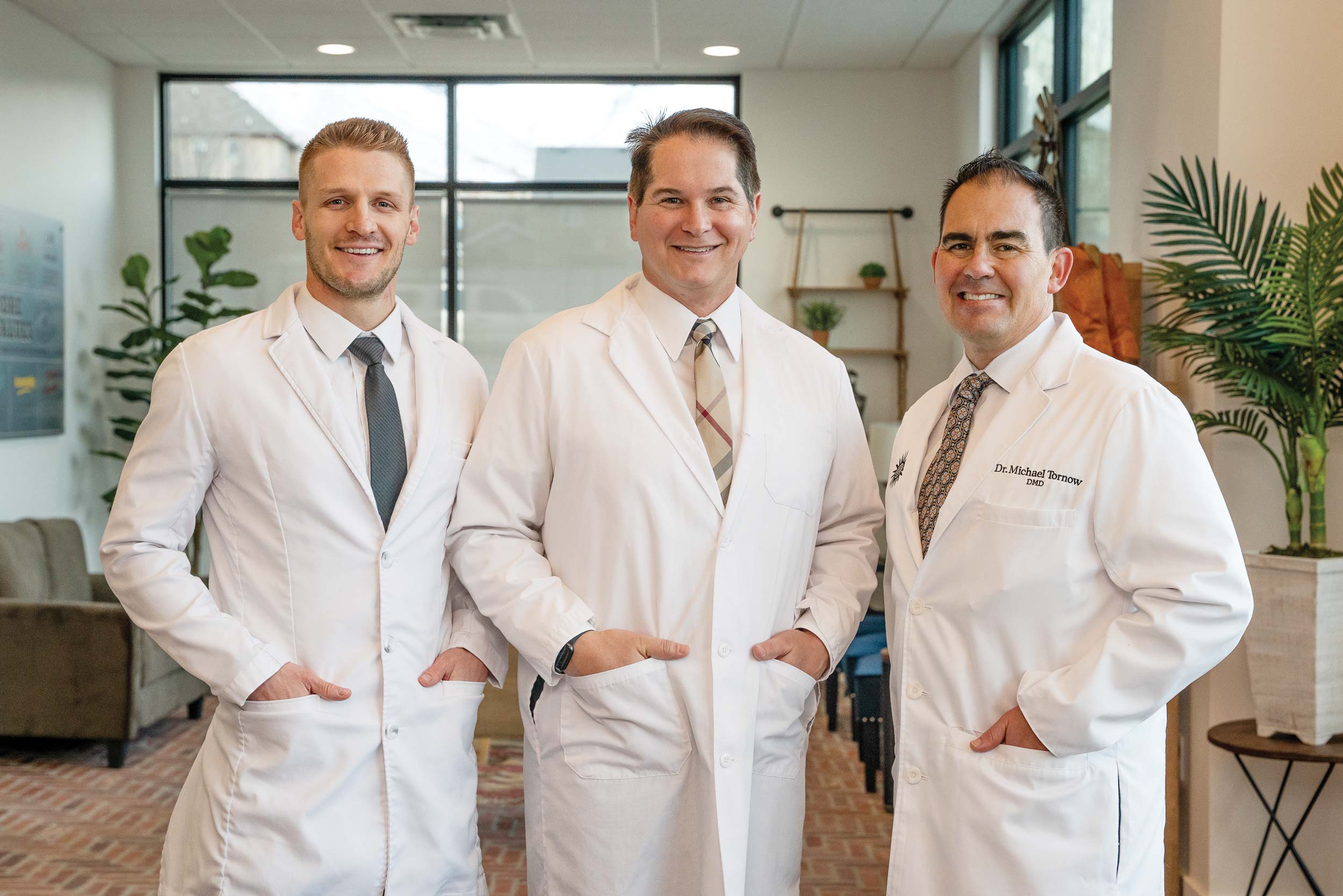 Meet the managing partners: Dr. Dallin DeLoach, Dr. Tom Chamberlain, and Dr. Michael Tornow. The smiling doctors are wearing white lab coats. They are standing side-by-side smiling pleasantly at the camera.