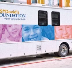 Buses for St. David's Foundation, one of the largest school-based mobile dental programs in the U.S., are lined up along a building to offer free dental care to kids. The buses are white with colorful duotone images of smiling children from all races and ages.