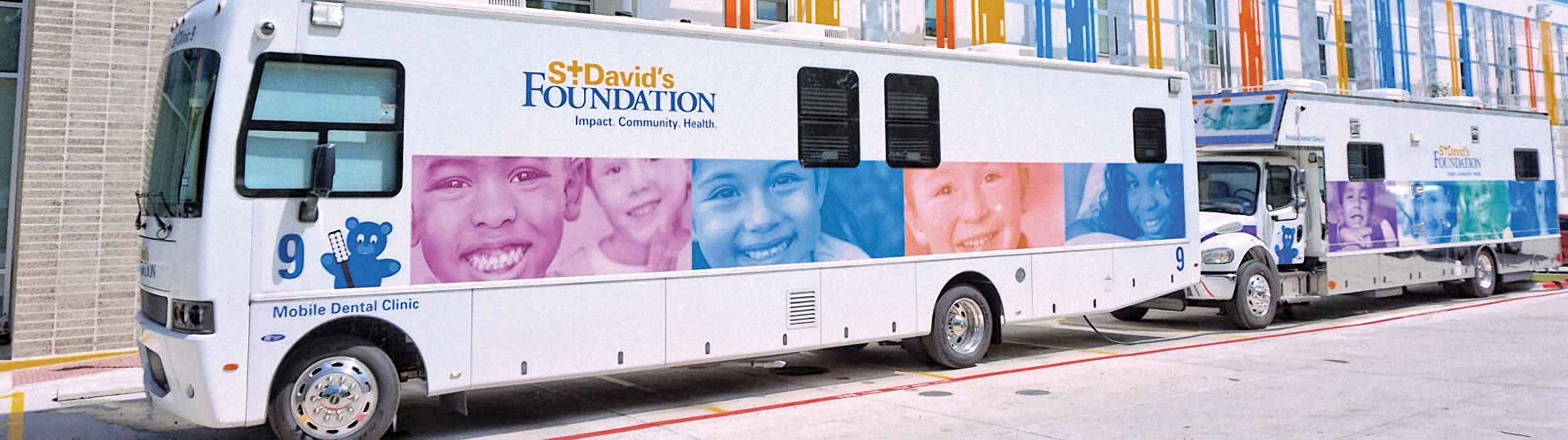 Buses for St. David's Foundation, one of the largest school-based mobile dental programs in the U.S., are lined up along a building to offer free dental care to kids. The buses are white with colorful duotone images of smiling children from all races and ages.