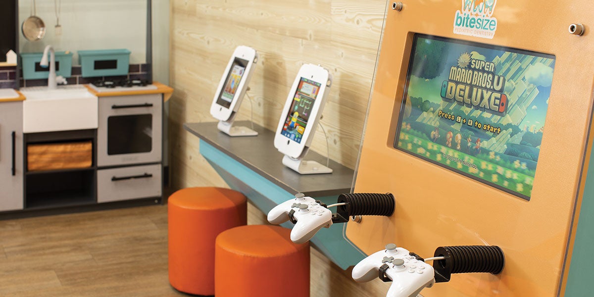 With an eye to short attention spans, the welcoming area has an iPad and Nintendo Switch station and a play kitchen. The kitchen sits on a back wall while the iPad and Nintendo Switch station are on the adjoining wall.