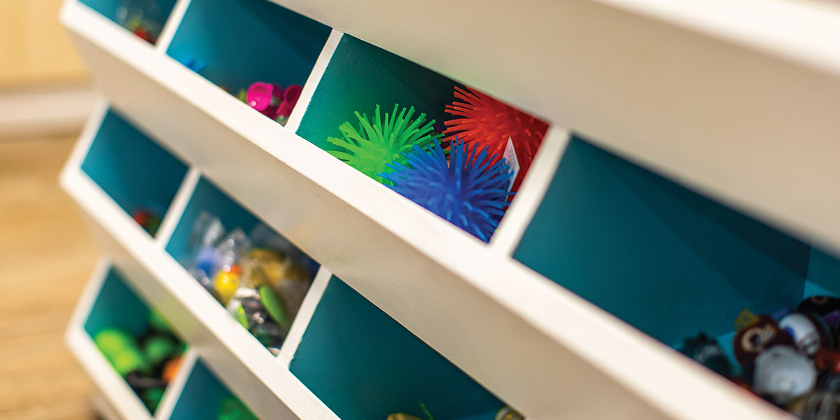 The prize wall, built by Josh, offers 16 cubbies filled to the brim with fun prize selections for kids to take home after their appointments. The cubbies are white on the outside with a beautiful ocean blue on the inside.