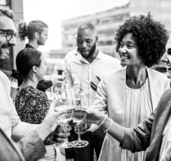 Group of business people and friends gathered for a dental roadshow happy hour event. Four people with different ethnic backgrounds are clinking white wine glasses.