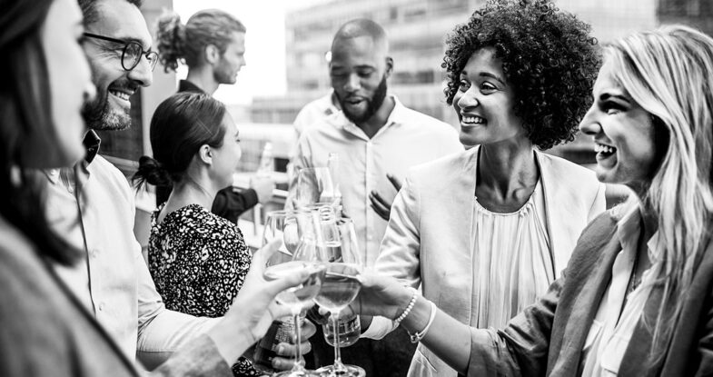 Group of business people and friends gathered for a dental roadshow happy hour event. Four people with different ethnic backgrounds are clinking white wine glasses.