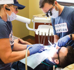 Dr. William Winterholler and a team member examine a Veteran's teeth. The Veteran is laying down in the dental chair, while the two team members continue their examination.