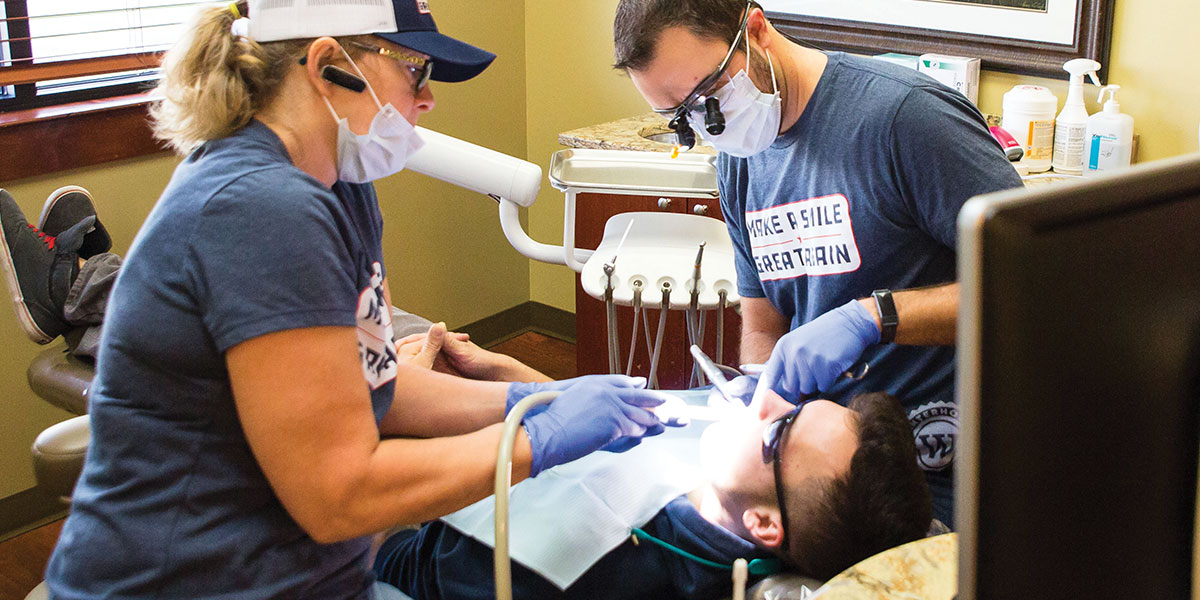 Dr. William Winterholler and a team member examine a Veteran's teeth. The Veteran is laying down in the dental chair, while the two team members continue their examination.