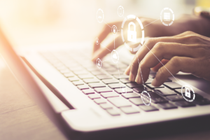 Cyber security depicted through a woman's hands on a keyboard of a laptop. Superimposed over the image are graphics of locks, emails, clouds, and other icons symbolizing our online lives.